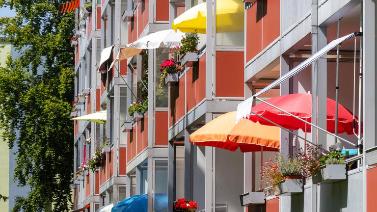 Eine Häuserreihe mit Balkonen, auf denen Sonnenschirme aufgeklappt stehen.