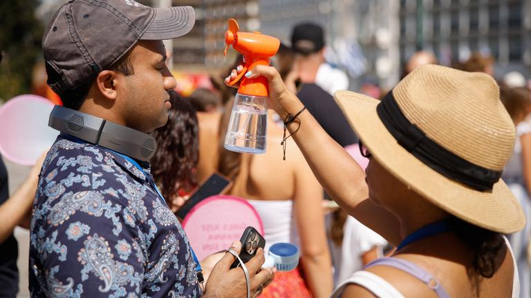 Zwei Menschen versuchen sich mit kleinen Handventilatoren und Wasser abzukühlen.