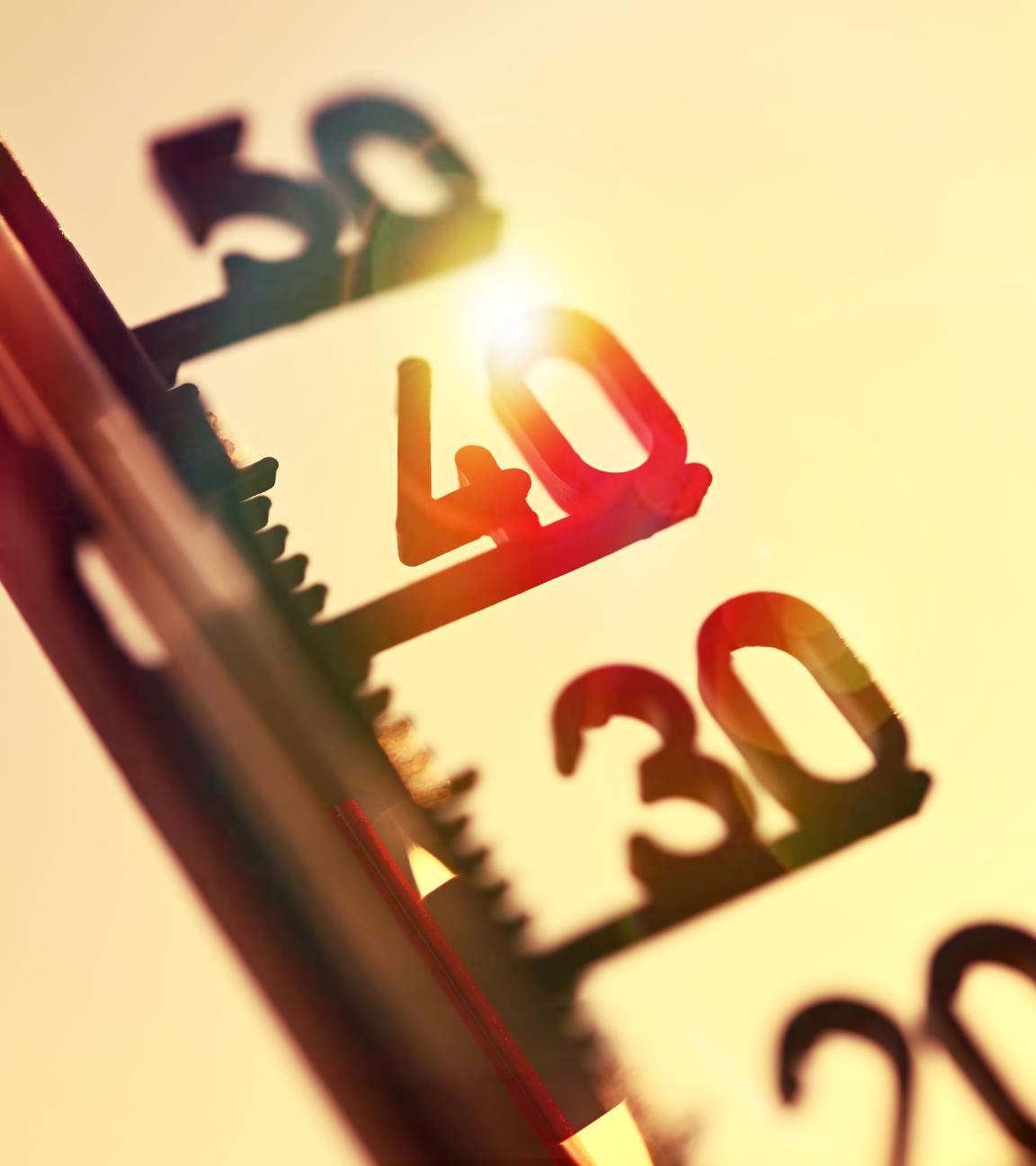 Thermometer zeigt hohe Temperaturen an.Im Hintergund steht die Sonne am Himmel.