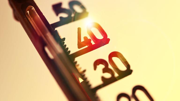Thermometer zeigt hohe Temperaturen an.Im Hintergund steht die Sonne am Himmel.
