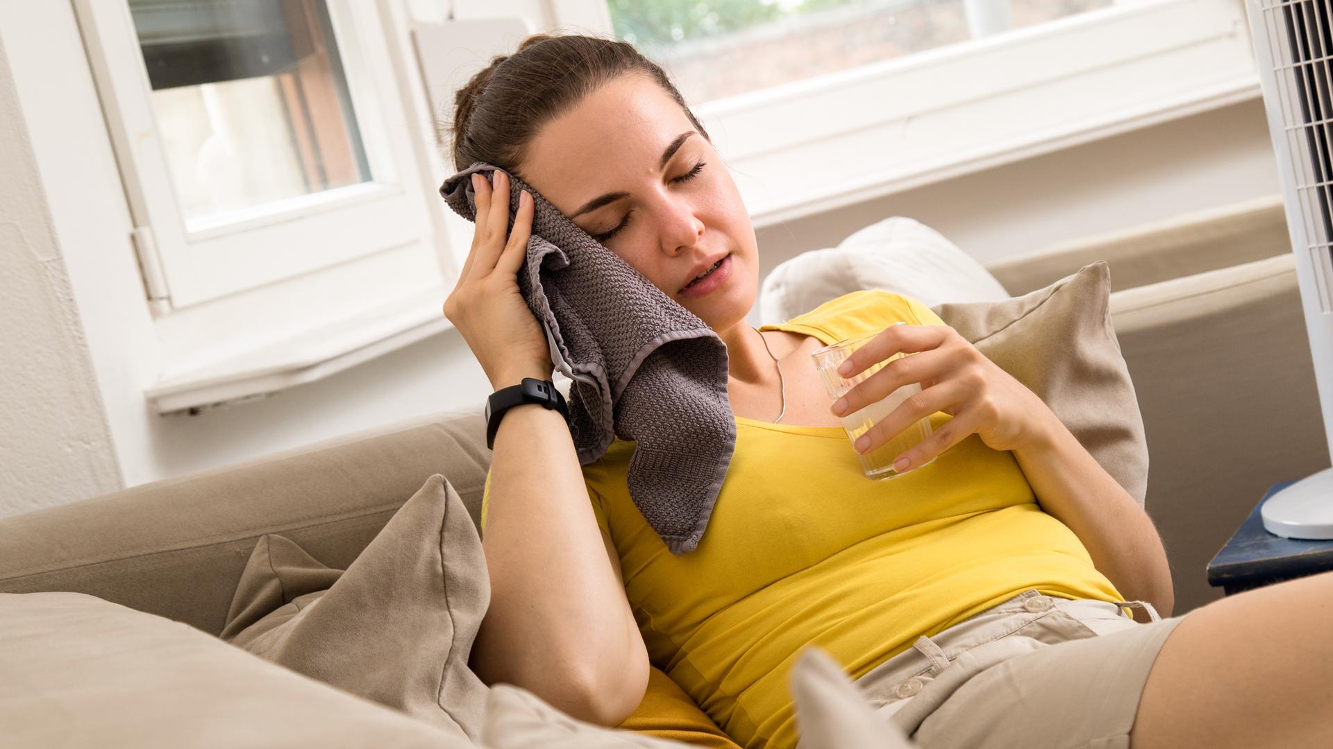 Frau hält sich Handtuch an die Stirn.