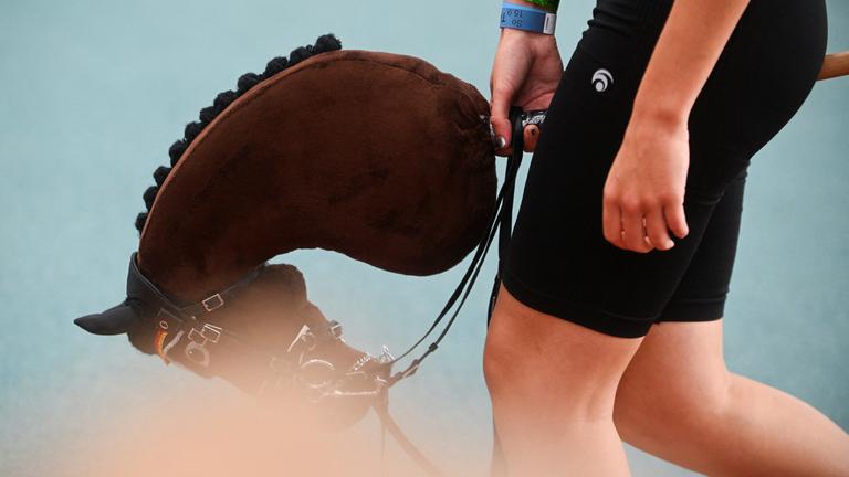 Eine Person ist ab dem Unterkörper zu sehen, sie hat ein Steckenpferd zwischen den Beinen. 