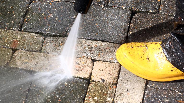 Mann mit gelben Gummistiefeln reinigt Pflastersteine mit Hochdruckreiniger.