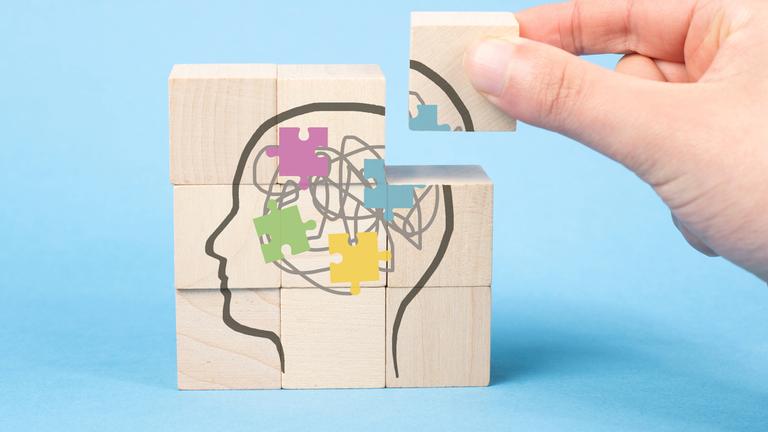 Auf neun Holzwürfeln ist das Bild eines Gehirns zu sehen. Eine Hand setzt den letzten Stein ein.