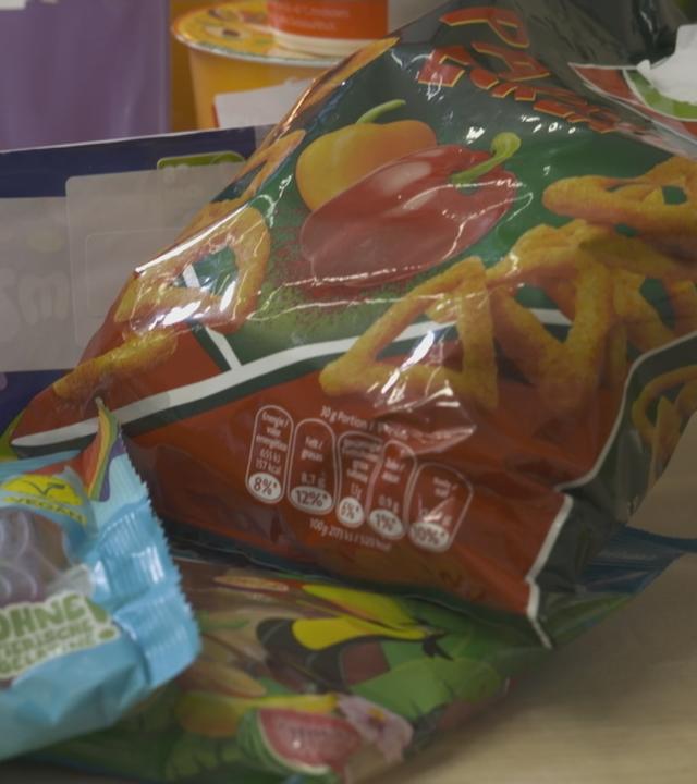 Hochverarbeitete Lebensmittel - Chips, Joghurt, Gummibärchentüten auf einem Tisch