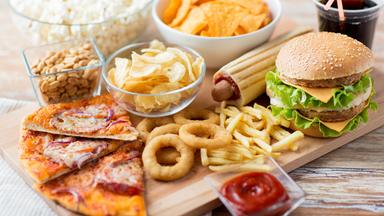 Verschiedene Fast Food Gerichte liegen auf einem Tisch, darunter Chips, Pizza, Pommes und Burger.