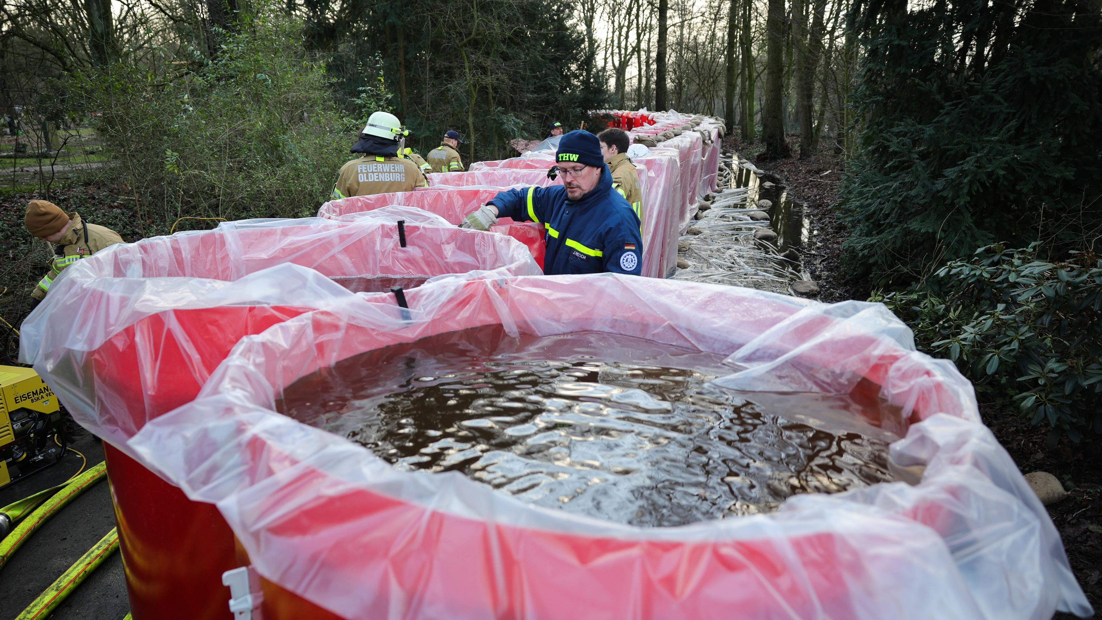 Mitarbeiter von THW und der Feuerwehr Oldenburg befüllen Elemente eines mobilen Notdeichs mit Wasser am 03.01.2024.