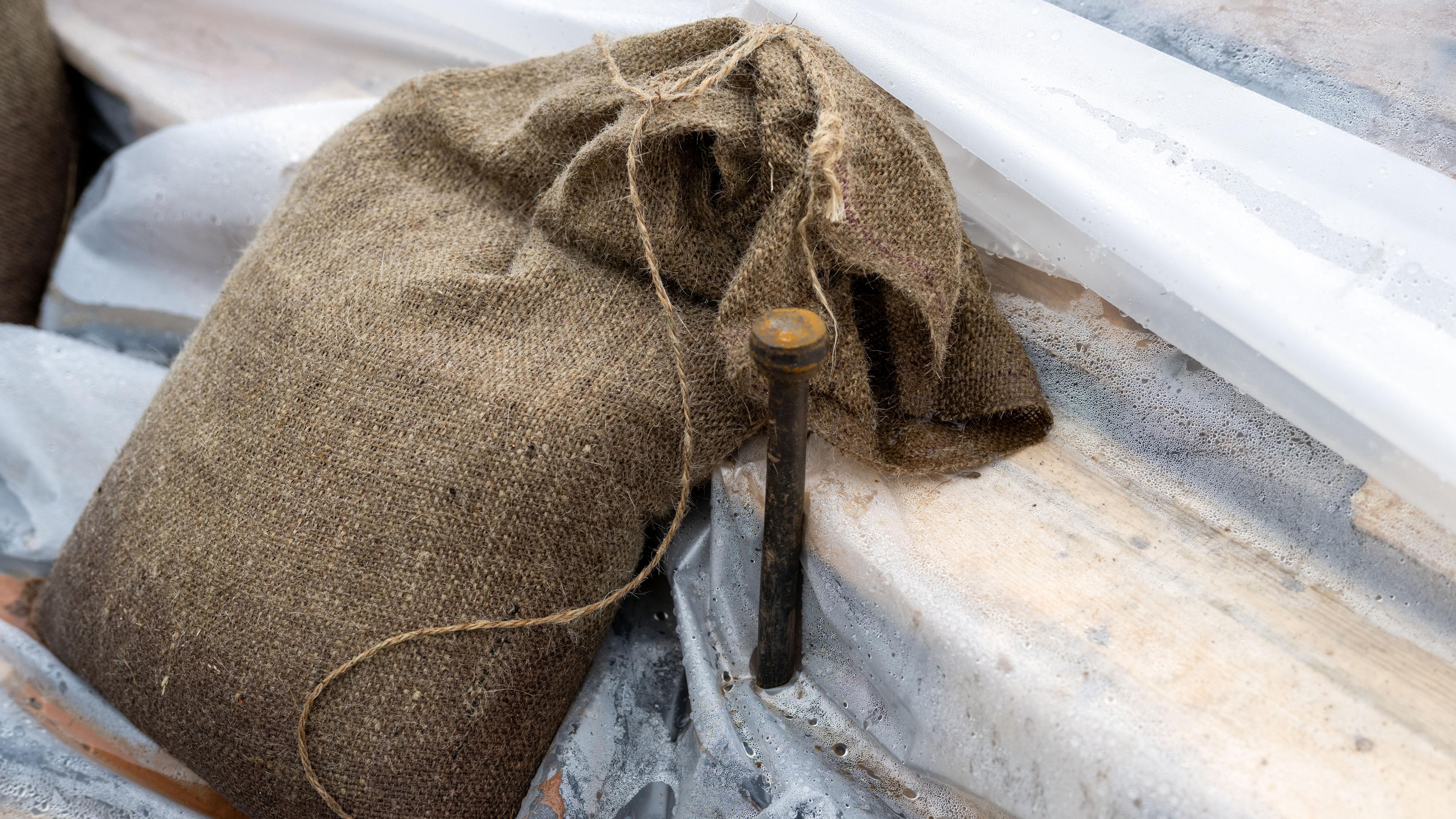 Ein Sandsack liegt auf einer Plane, ein Erdnagel sorgt für zusätzliche Stabilität.