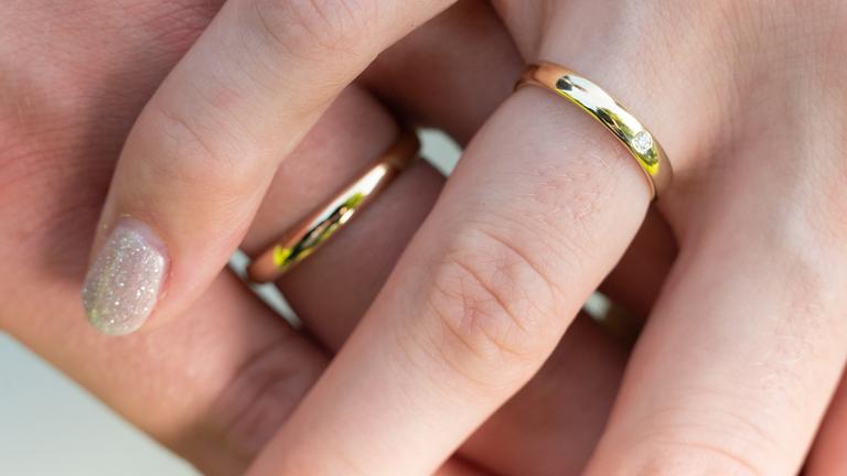 Zwei Hände mit goldenen Eheringen liegen übereinander.