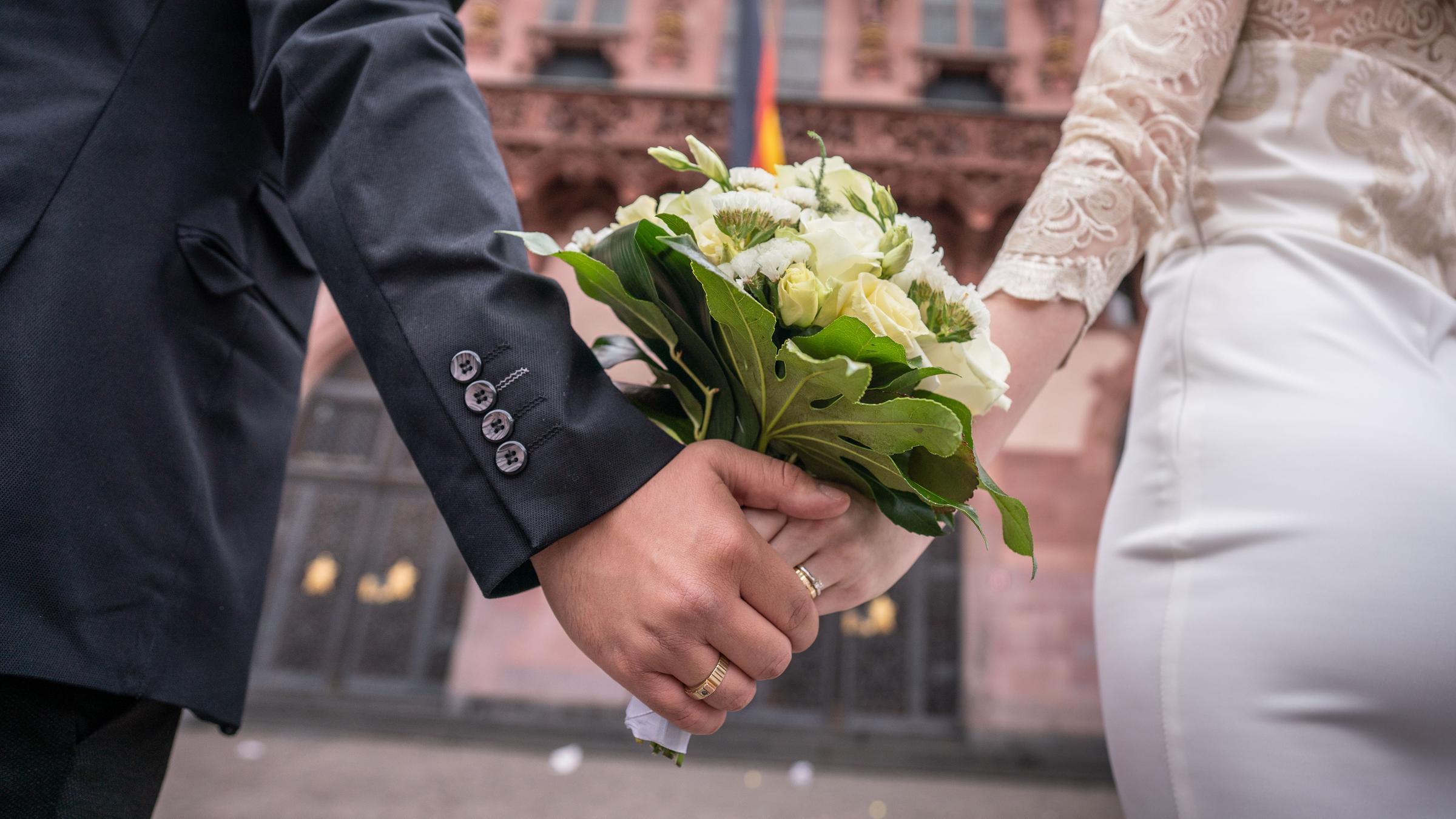 Ein Ehepaar steht händehaltend vor dem Standesamt
