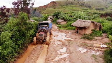 Ein Weg voller Schlamm, über den ein Traktor fährt. Daneben steht eine Hütte.