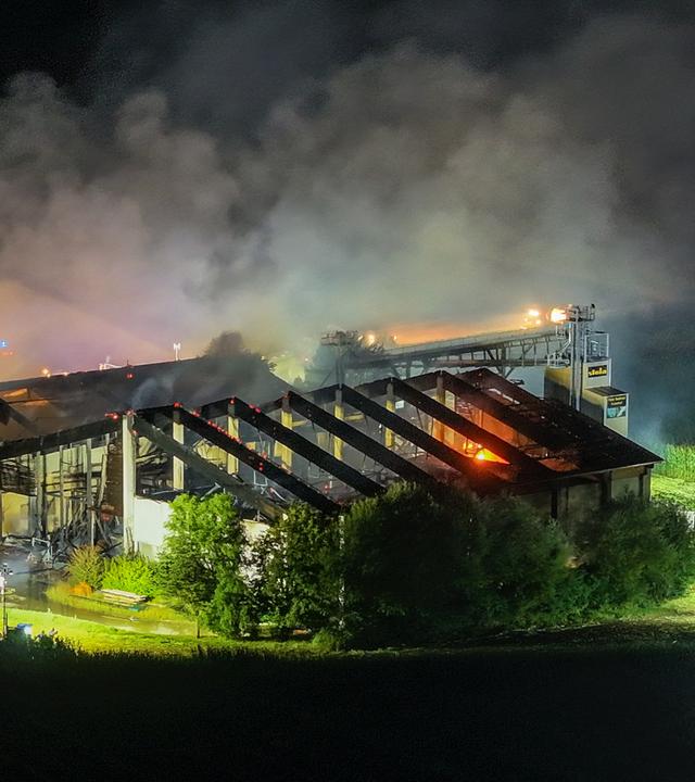 Starker Brand in einem Schweinestall während der Nacht. Über dem Gebäude steigen große Rauchwolken auf, Teile des Dachs sind zerstört.