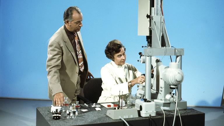 Farbfoto von Hoimar von Ditfurth, der einer Wissenschaftlerin über die Schulter guckt.