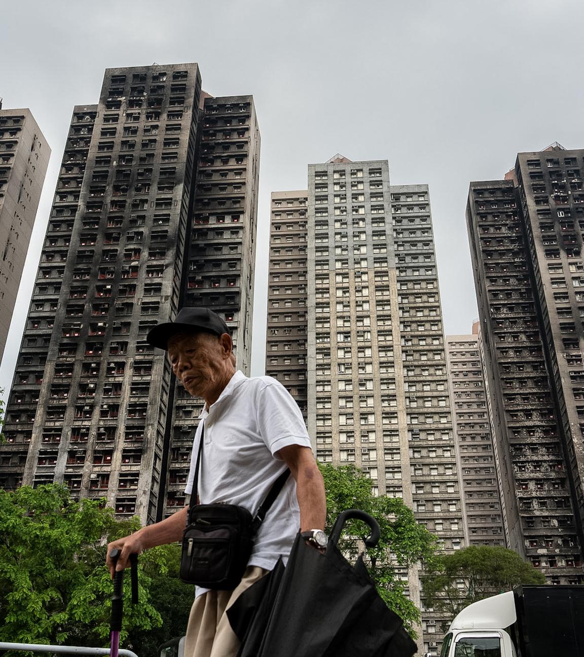 Eine Person geht im Stadtteil Tai Po in Hongkong an den vom Feuer zerstörten Wohntürmen des Wang Fuk Court Apartmentkomplexes vorbei.