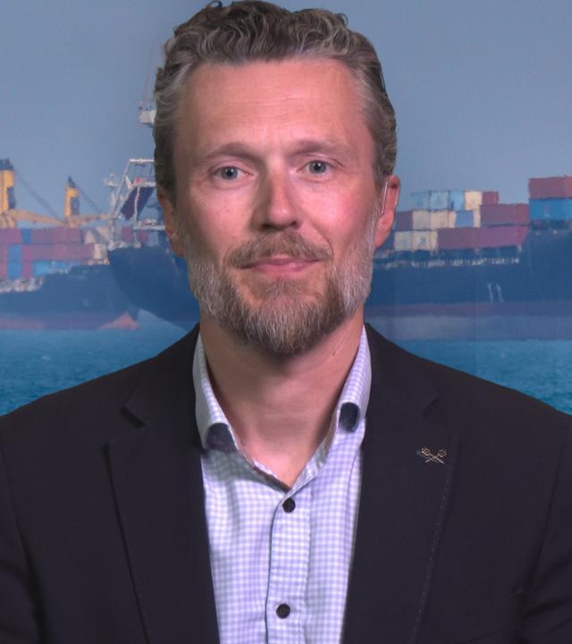 Johannes Peters in einem Anzug gekleidet mit dem Hamburger-Hafen als Hintergrund Bild.