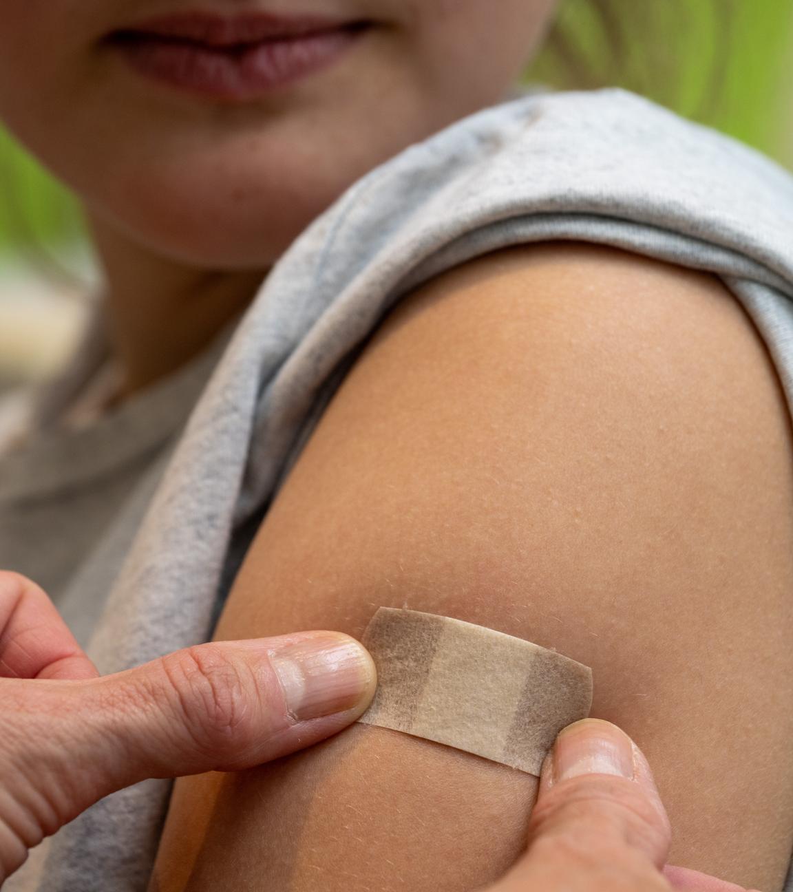 Ein junges Mädchen, dass ein Pflaster auf ihrem Oberarm aufgetragen bekommt.