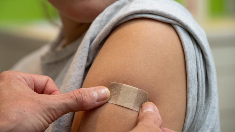 Ein junges Mädchen, dass ein Pflaster auf ihrem Oberarm aufgetragen bekommt.