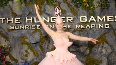 Das Bild zeigt Schauspielerin Elle Fanning in einem pinken Kleid mit ausgefallenem Kopfschmuck. Sie nimmt die Pose einer Ballerina ein.