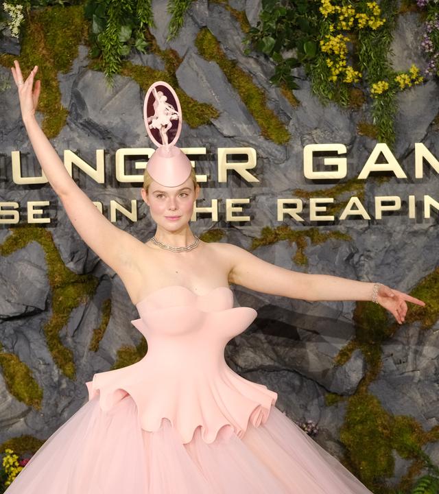 Das Bild zeigt Schauspielerin Elle Fanning in einem pinken Kleid mit ausgefallenem Kopfschmuck. Sie nimmt die Pose einer Ballerina ein.