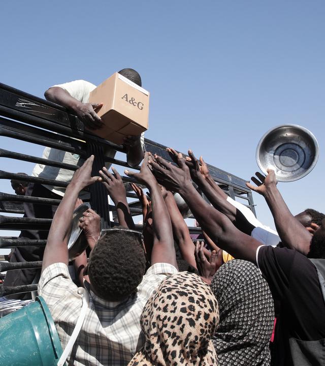 Sudanesische Familien strecken ihre Hände aus, während Mitarbeiter von Hilfsorganisationen Lebensmittel verteilen