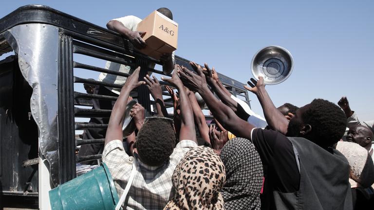 Sudanesische Familien strecken ihre Hände aus, während Mitarbeiter von Hilfsorganisationen Lebensmittel verteilen