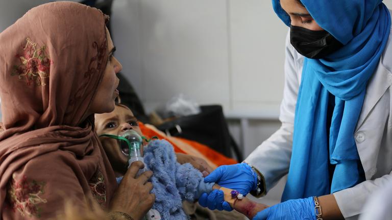 Latifa Bakkar versucht, ihrem schwer unterernährten 2½-jährigen Sohn Abu Bakar Sauerstoff zu verabreichen, während eine Krankenschwester ihm im Indira-Gandhi-Kinderkrankenhaus in Kabul, Afghanistan, am  15. 2. 2026, eine intravenöse Kanüle in den Arm legt. 