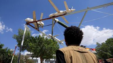 Eine Person geht auf einem Platz in Sanaa (Jemen an einer Ausstellung von Attrappen von Drohnen und Raketen aus Houthi-Produktion vorbei.
