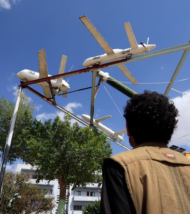 Eine Person geht auf einem Platz in Sanaa (Jemen an einer Ausstellung von Attrappen von Drohnen und Raketen aus Houthi-Produktion vorbei.