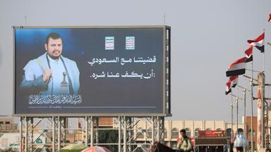 Jemenitische Flaggen wehen neben einer digitalen Werbetafel, die den Huthi-Anführer Abdul-Malik al-Huthi sowie den arabischen Schriftzug „Unser Streit mit Saudi-Arabien besteht darin, dass es seine Aggressionen gegen uns einstellt“ zeigt.