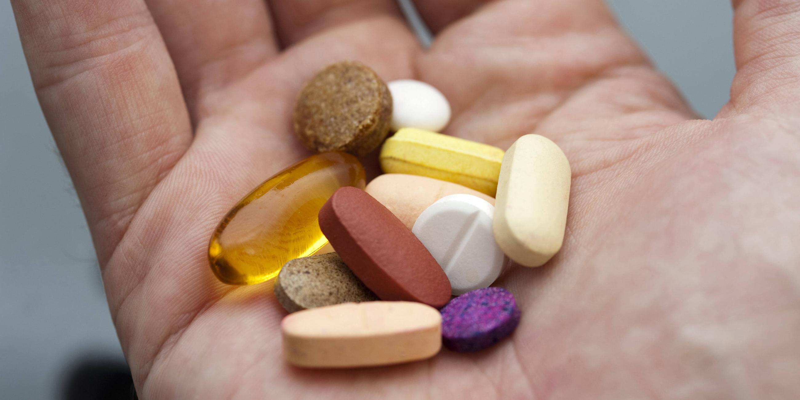 Die offene Hand eines Mannes mit einem Cocktail aus verschiedenen Tabletten und Pillen, Medikamenten und Nahrungsergänzungsmitteln.