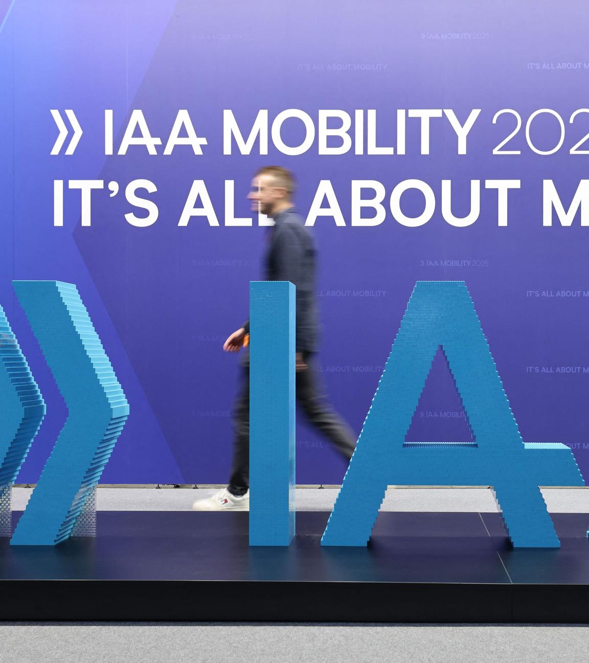 Das große Logo der IAA. Dahinter läuft ein Mann lang. An der Wand steht:IAA Mobility 2025, it´s all about mobility