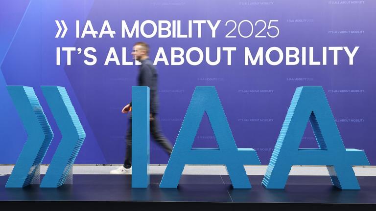 Das große Logo der IAA. Dahinter läuft ein Mann lang. An der Wand steht:IAA Mobility 2025, it´s all about mobility