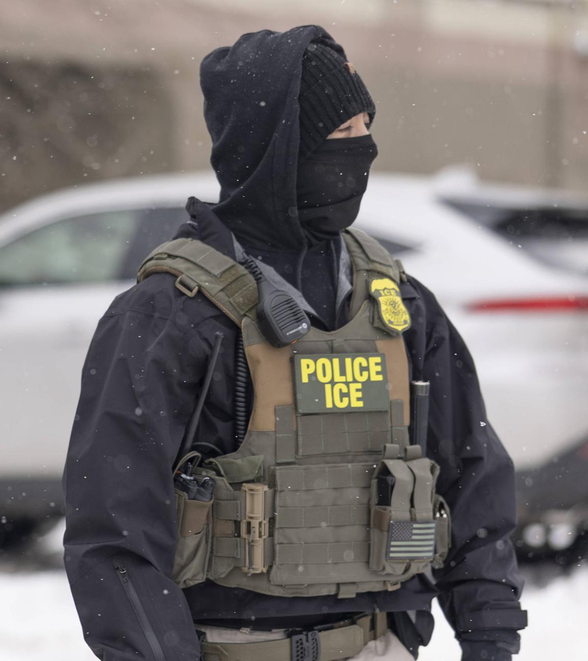 Ein Polizist und im Hintergrund unscharf eine Frau während eines ICE-Einsatzes nahe der Karmel Mall am 10.12.2025 in Minneapolis, USA.