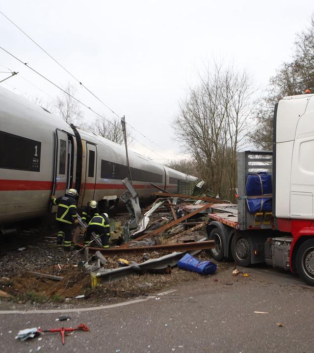 Ein Polizist sieht zu, wie Feuerwehrleute an der Unfallstelle zwischen einem LKW und einem ICE (InterCity Express) der Deutschen Bahn an einem Bahnübergang im Hamburger Stadtteil Rönneburg arbeiten
