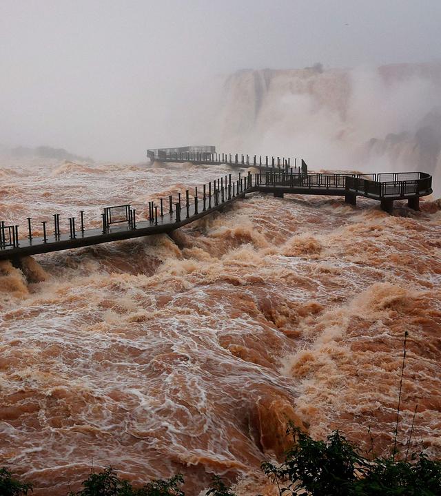 Gesamtansicht des Besucherwegs an den Iguazú-Wasserfällen über einer starken Strömung aufgenommen.