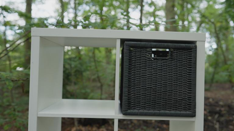 weißes Ikea-Regal mit schwarzen Flechtkorb in einem Regalfach steht im Wald