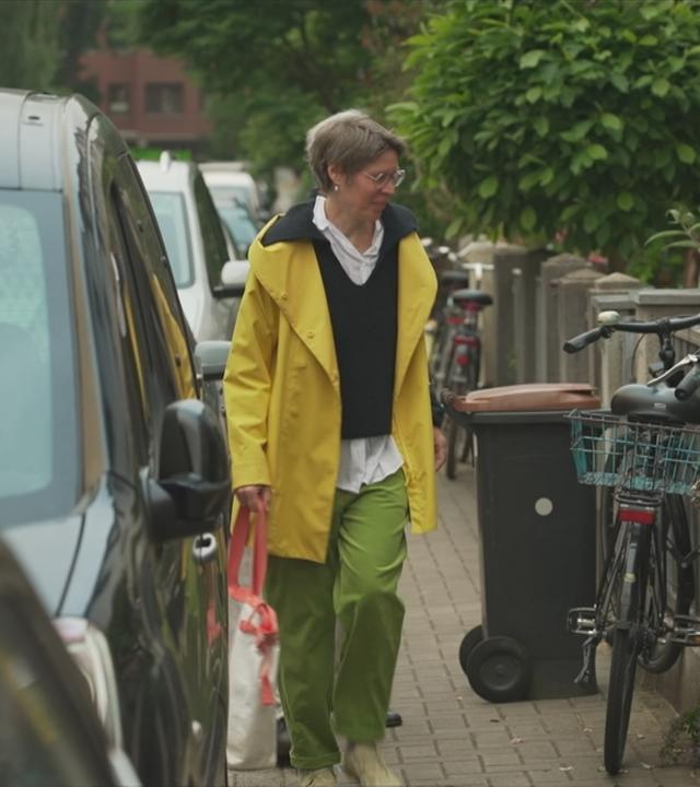 Fußgängerin quetscht sich an auf dem Gehsteig parkenden Autos vorbei.