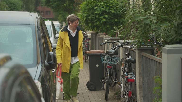 Fußgängerin quetscht sich an auf dem Gehsteig parkenden Autos vorbei.