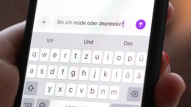 Eine Person hält ein Smartphone in der Hand, auf dem eine Suchanfrage mit der Frage «Bin ich müde oder depressiv?» in einem KI-Chatfenster zu sehen ist. 