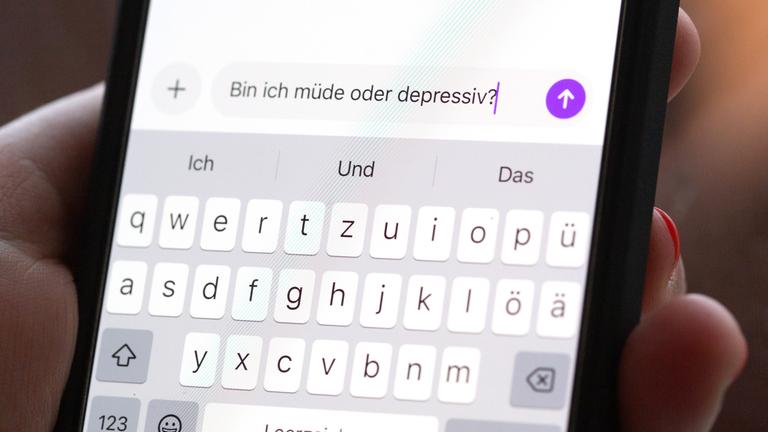 Eine Person hält ein Smartphone in der Hand, auf dem eine Suchanfrage mit der Frage «Bin ich müde oder depressiv?» in einem KI-Chatfenster zu sehen ist. 