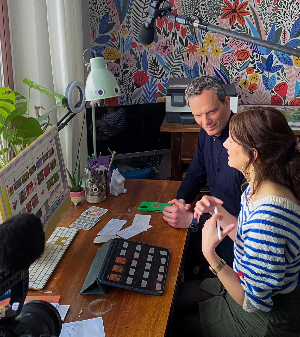Der Journalist Florian Neuhann und die Kinderbuchillustratorin Anne Behl sitzen nebeneinander an einem Schreibtisch vor einem Fenster.