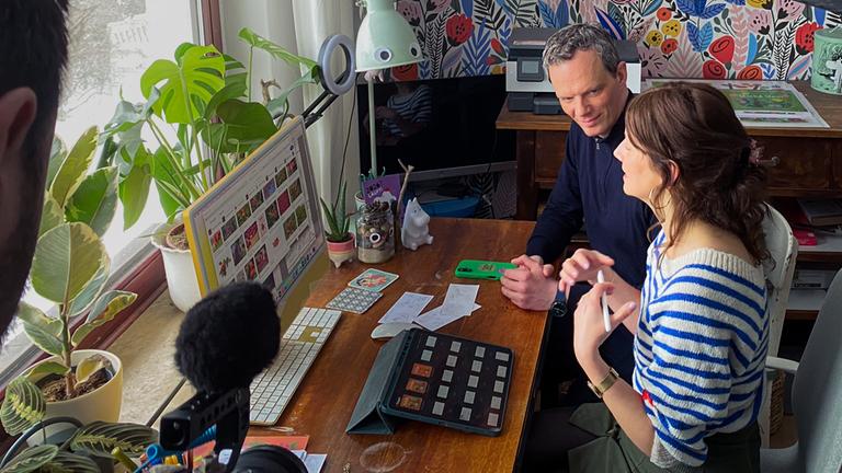 Der Journalist Florian Neuhann und die Kinderbuchillustratorin Anne Behl sitzen nebeneinander an einem Schreibtisch vor einem Fenster.