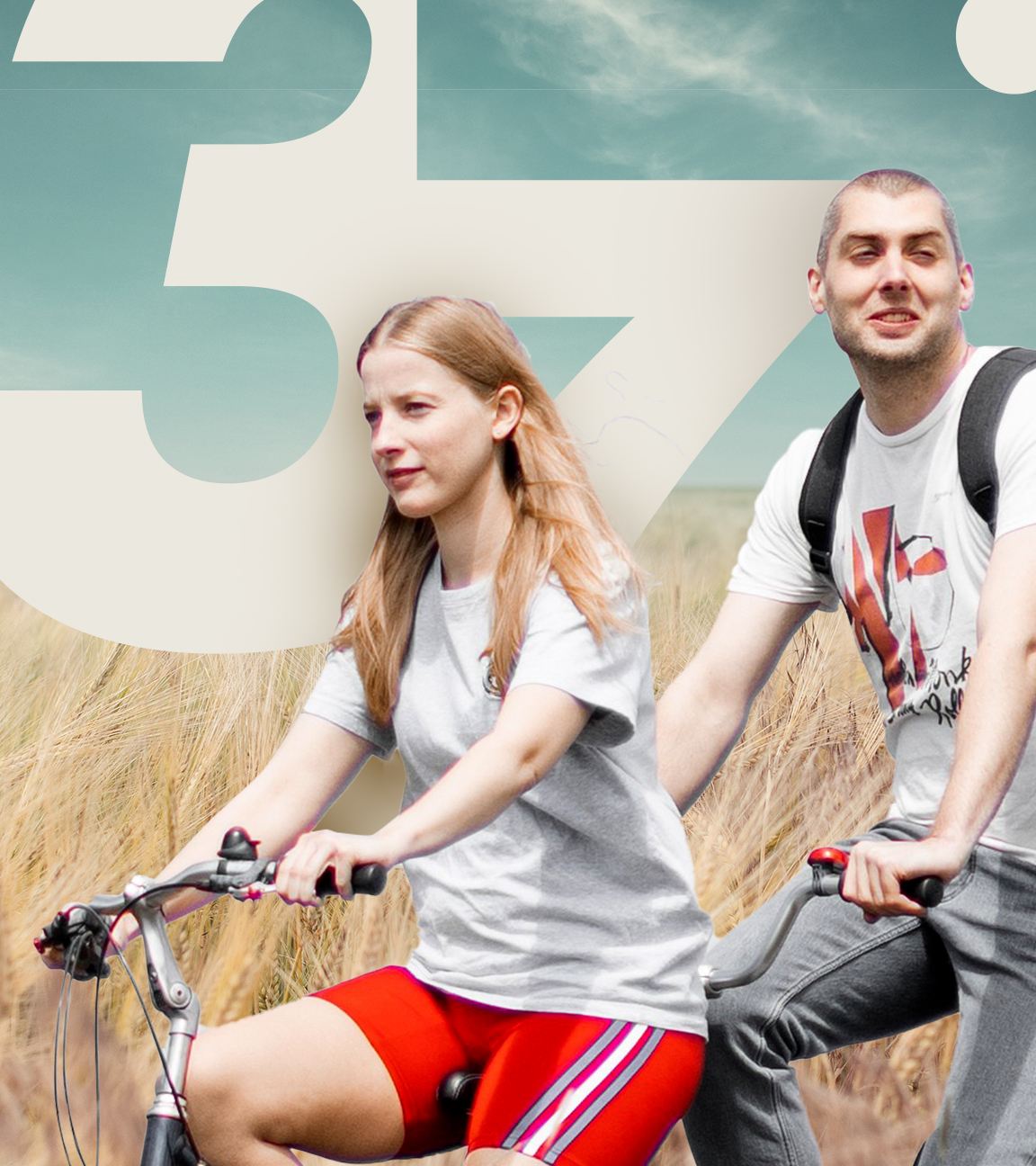 David und Cindy sitzen auf einem Tandem (Cindy vorn, David hinten) und fahren durch ein Feld, welches im Vordergrund zu sehen ist. Im Hintergrund sieht man einen bewölkten Himmel.