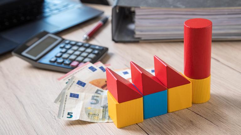 Bauklötze, Bargeld, ein Taschenrechner, ein Aktenordner und ein Laptop auf einem Tisch