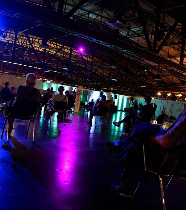 Menschen stehen bei der 1. Langen Nacht des Impfens am Impfzentrum Arena in Treptow an. Das Impfangebot des nächtlichen Impfens mit Musik richtet sich auch an Jugendliche ab 16 Jahren. Diese müssen unter anderem den von den Erziehungsberechtigten unterschriebenen Einwilligungsbogen vorlegen.