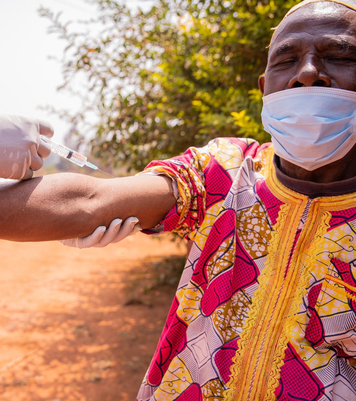 Ein afrikanischer Arzt impft einen älteren Mann mit einer Spritze am Arm. 