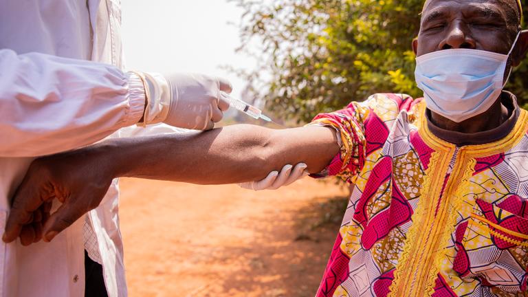 Ein afrikanischer Arzt impft einen älteren Mann mit einer Spritze am Arm. 