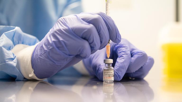 Eine Person zieht eine Spritze mit einem Impfstoff auf.