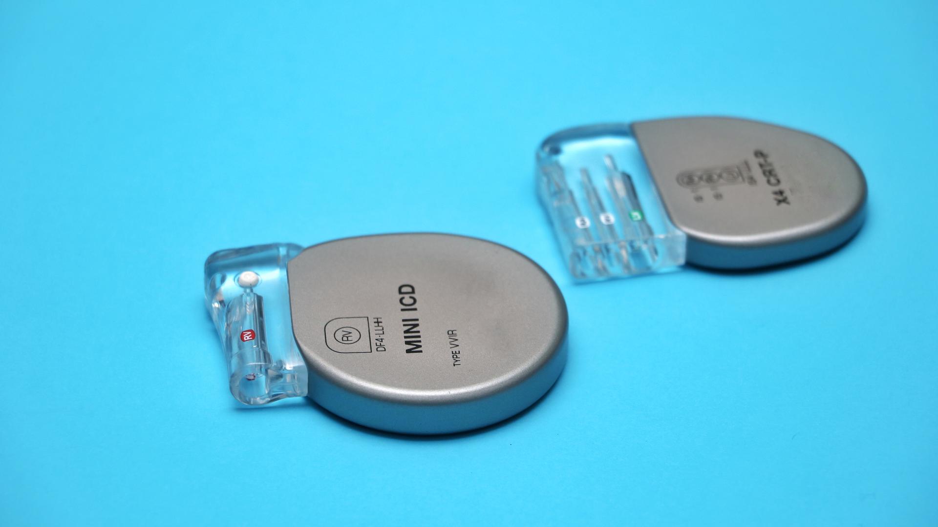 Zwei implantierbare Defibrillatoren liegen auf einer blauben Oberfläche.