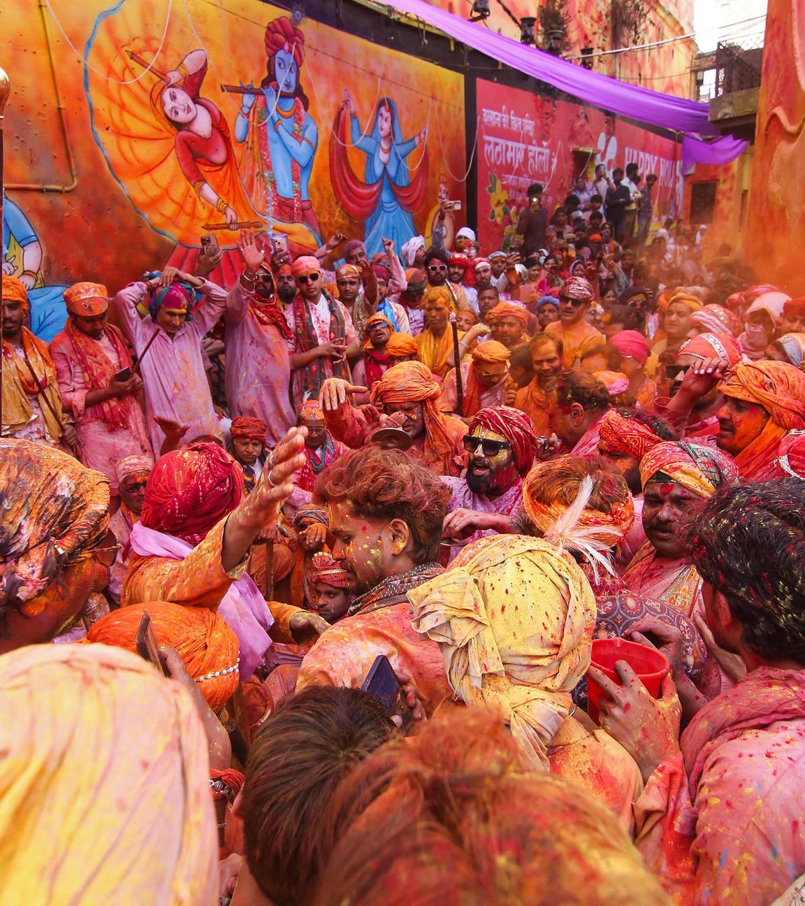Feiernde zelebrieren Lathmar Holi, das hinduistische Frühlingsfest der Farben, neben einem Wandgemälde von Lord Krishna in Barsana.